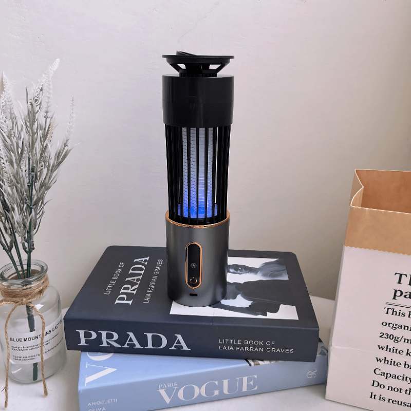 Electric mosquito zapper lamp with blue UV light, placed on luxury fashion books. Ideal for indoor mosquito control, stylish and chemical-free.
