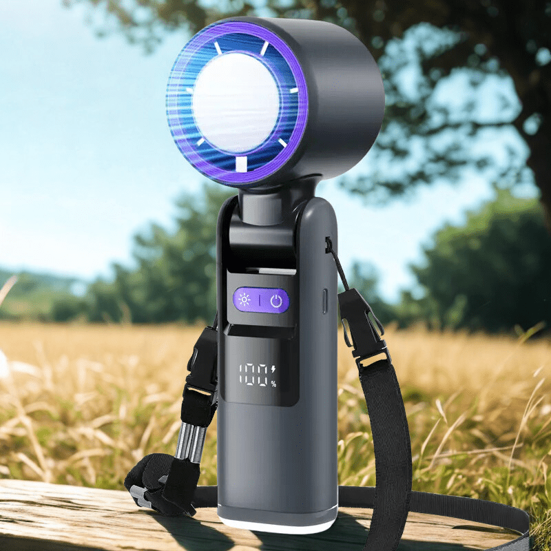 Handheld turbo fan with shoulder strap and digital display placed on a wooden bench in an outdoor field, designed for portable cooling during travel or summer activities - techynook