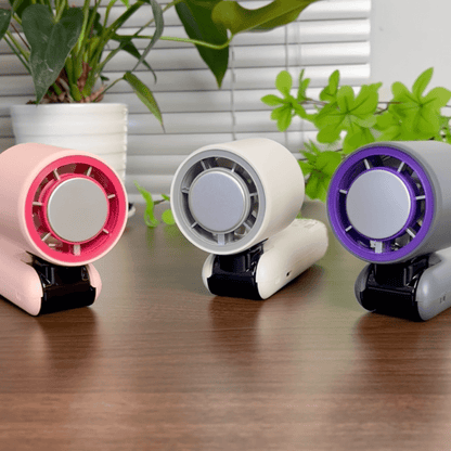 Three handheld turbo fans in pink, white, and grey with cooling system displayed on a wooden desk with indoor plants - techynook